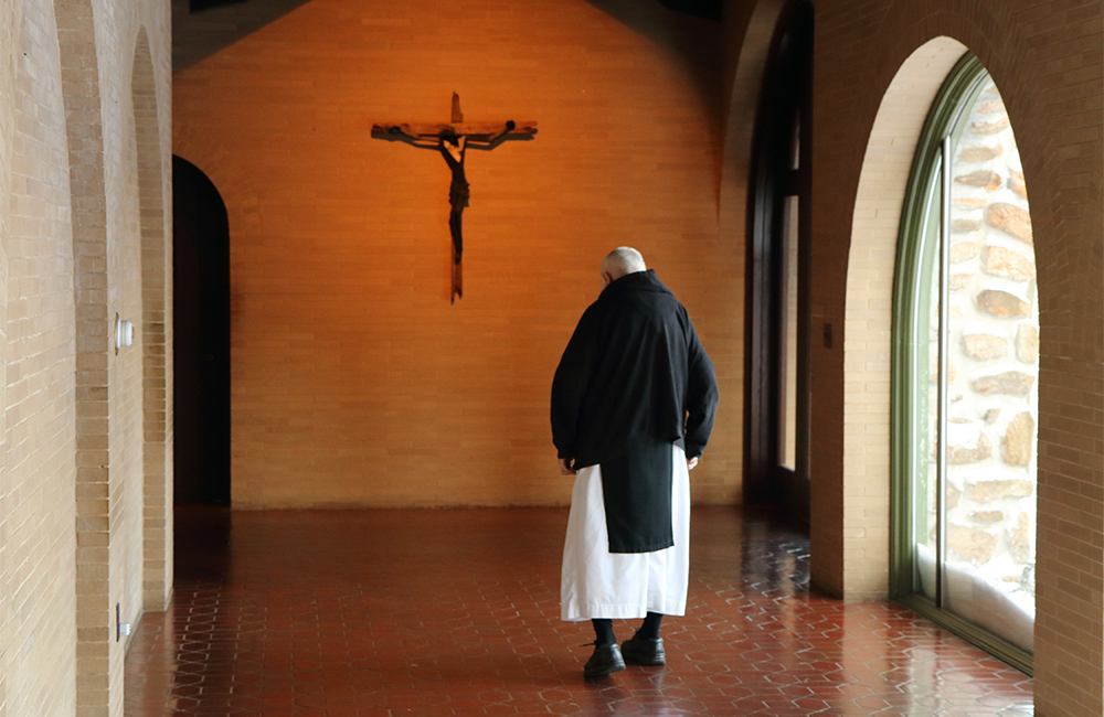 Monk gazing at crucifix in cloister walkway
