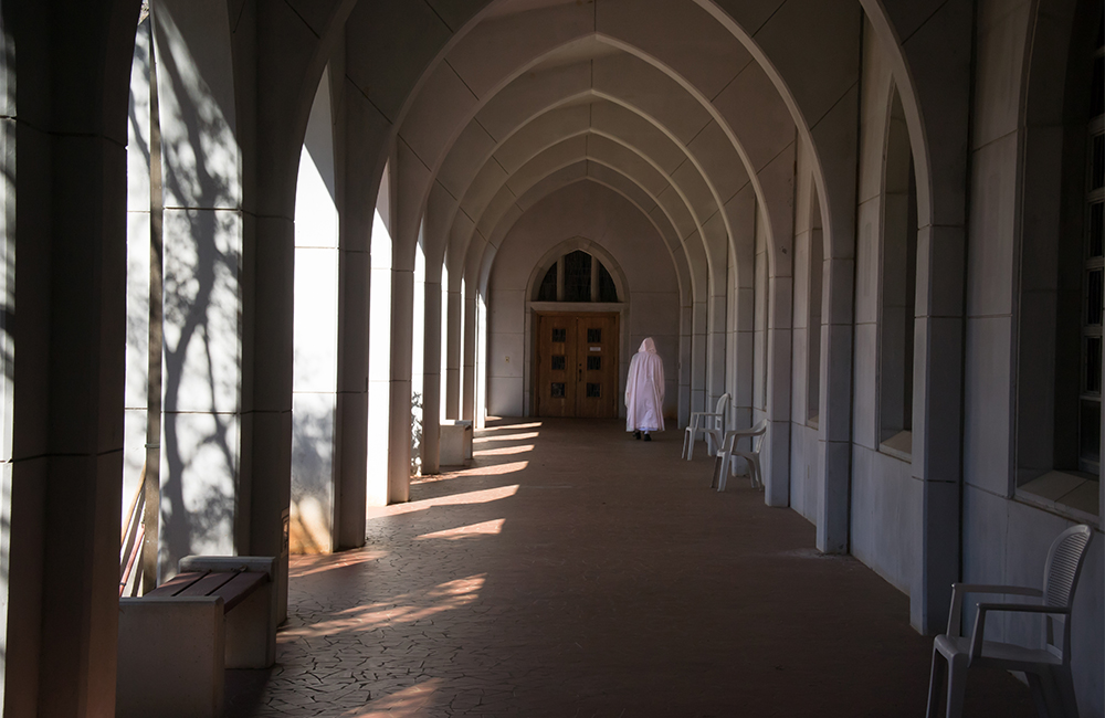 monk in white cowl in distance walking down sunlight cloister arcade