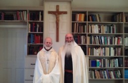Br. John and Abbot smiling in front of crucifix and bookcase