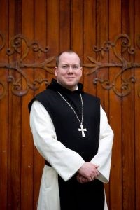 Trappist abbot standing in front of wooden door of Church