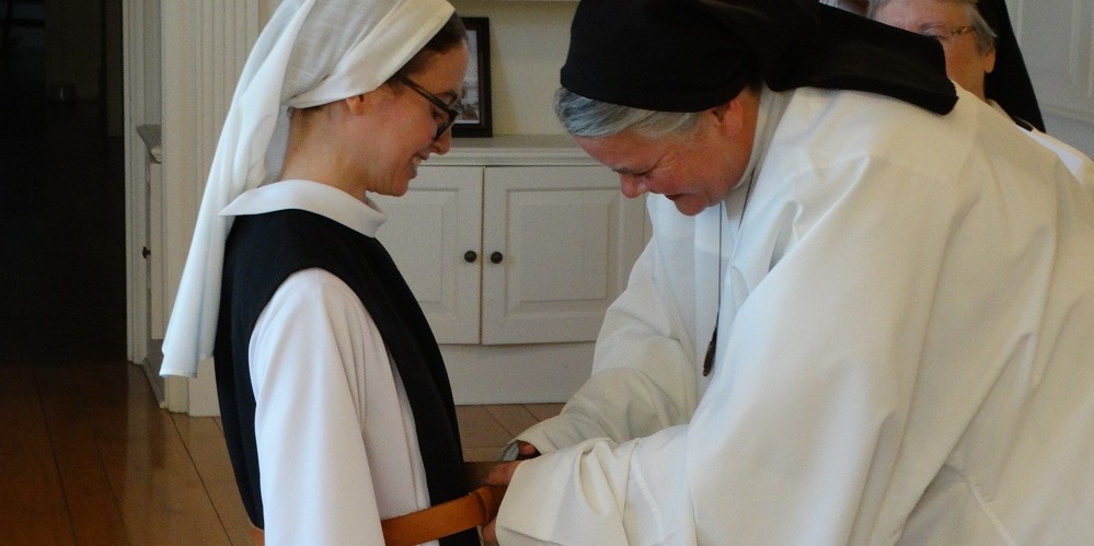 a nun kneeling and being clothed in belt of new habit by Mother Superior