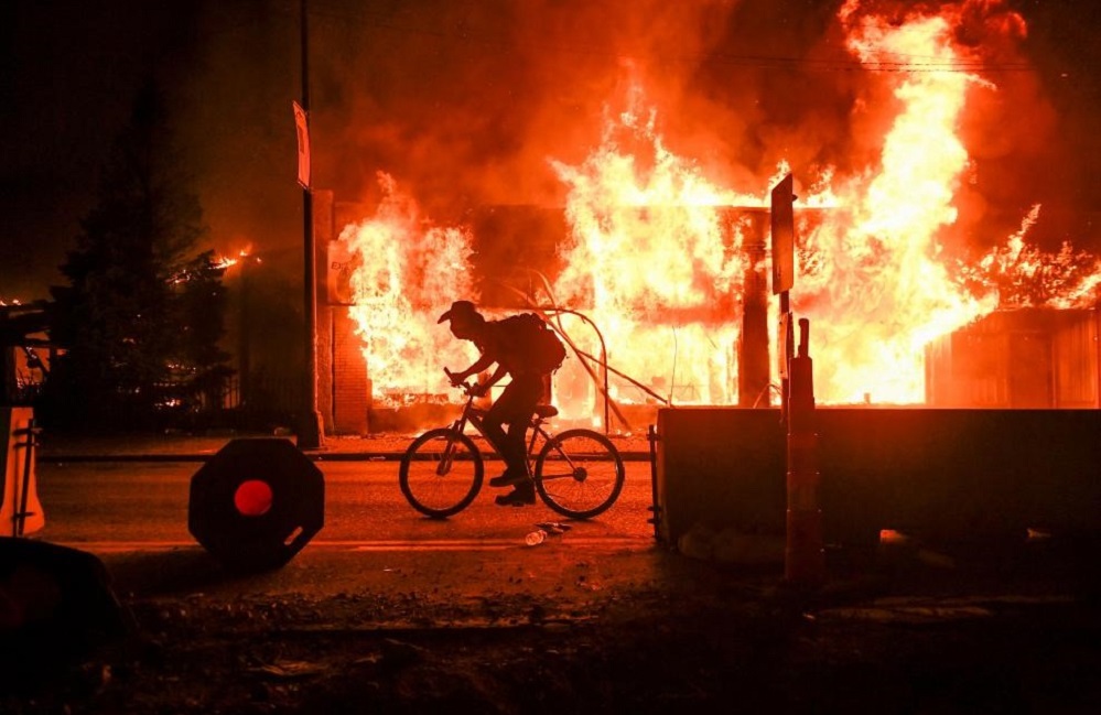 Man riding bike in front of burning building
