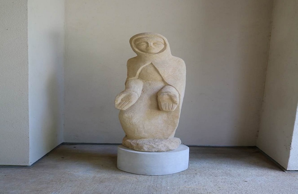 White stone sculpture of the Blessed Virgin Mary wearing cloak with hands held out by Dom Hubert Van Zellar