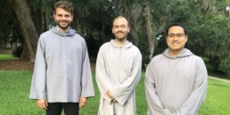 Three smiling men in grey smocks