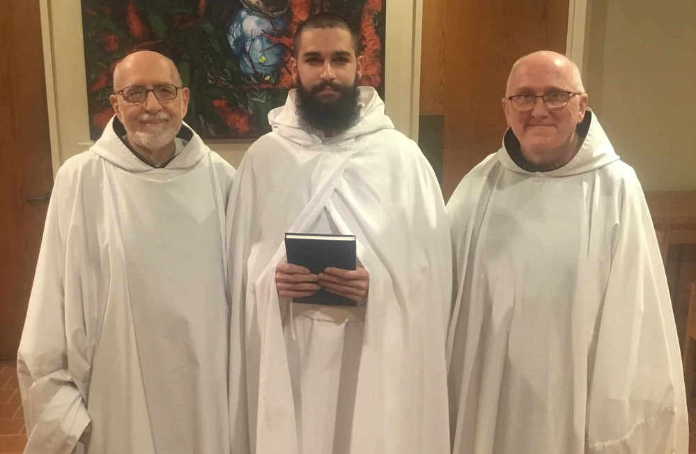 Br. Matthew enters novitiate, smiling holding book between abbot and Novice Director