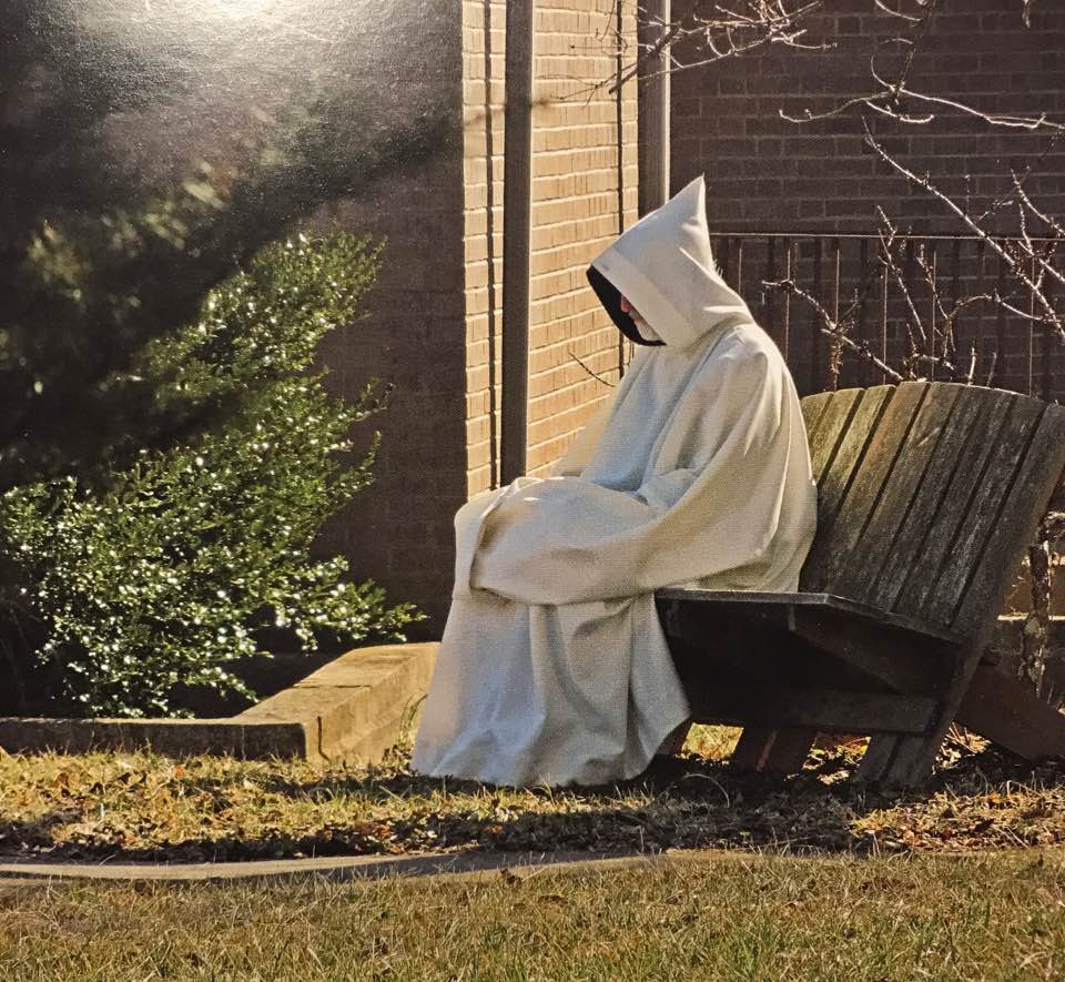 Trappist monk in white cowl sits and prays