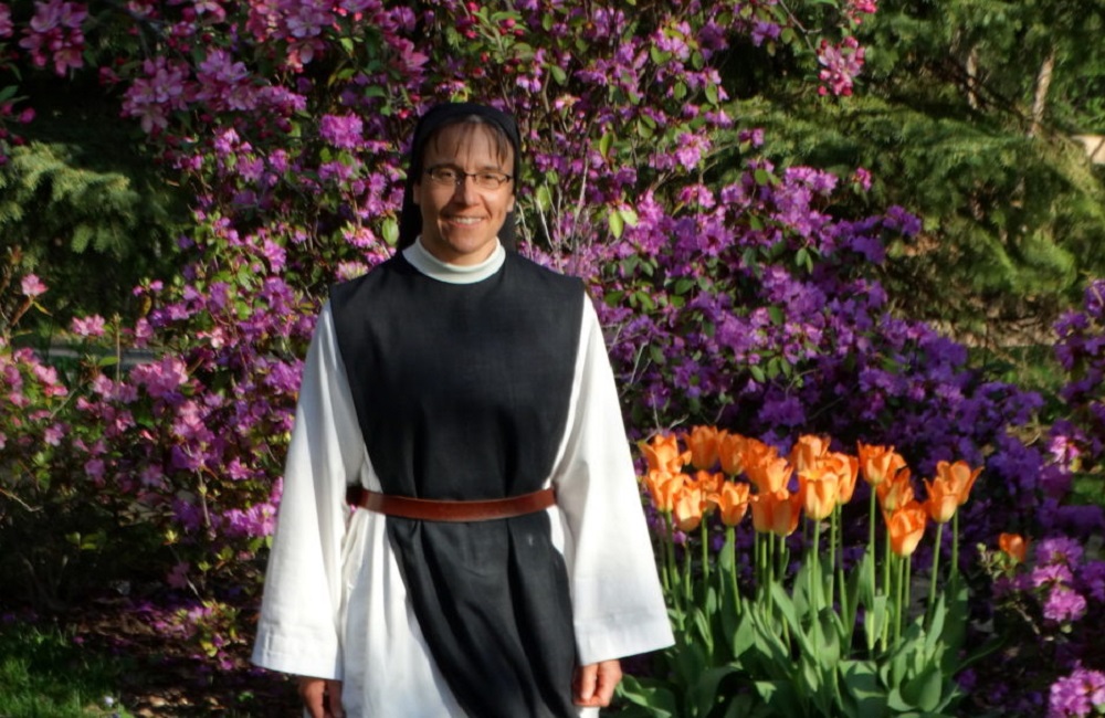 Sister Myra, a Trappistine nun standing in from of a garden of blooming flowers